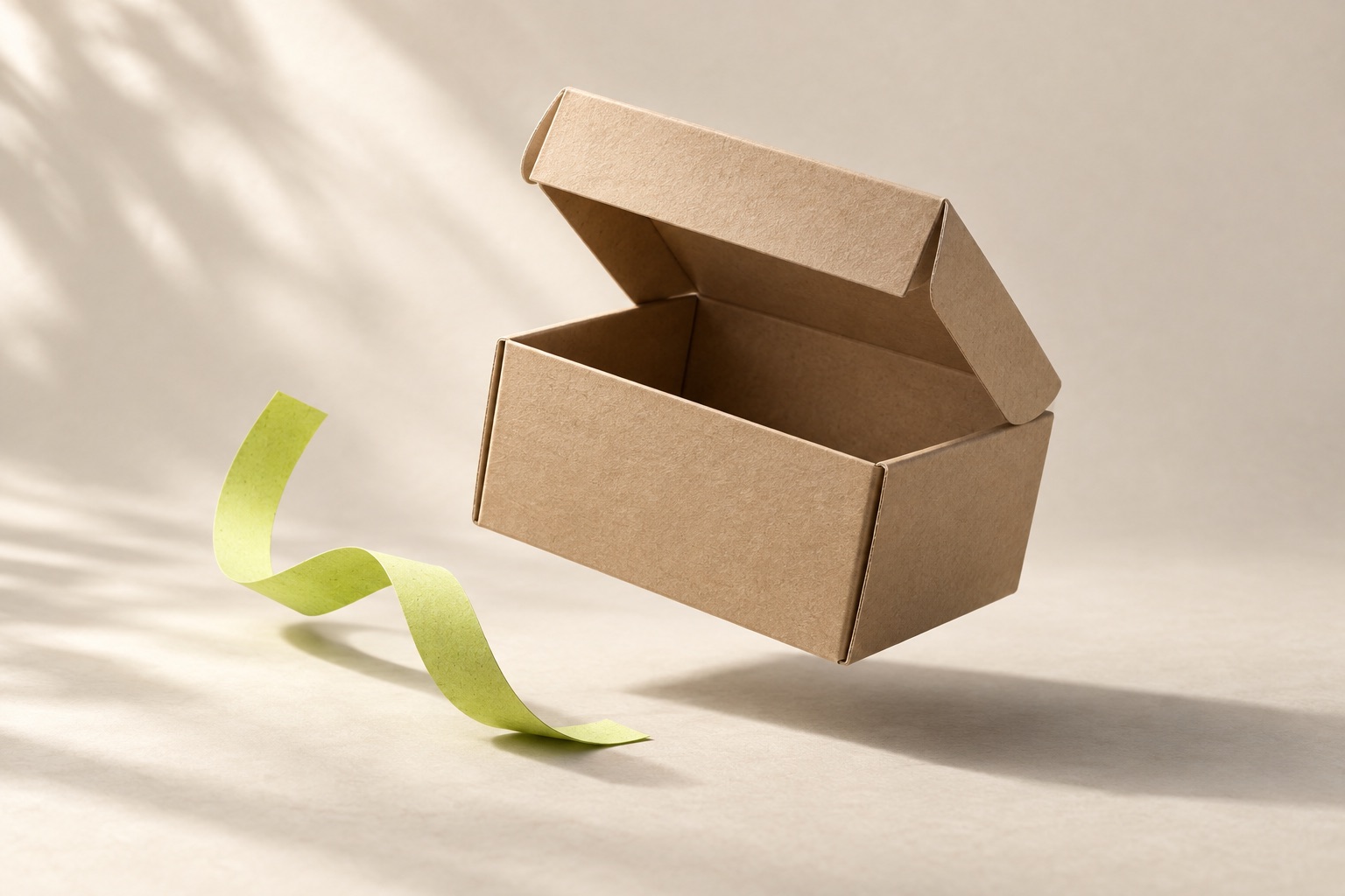 A kraft parcel box gently suspended over a warm paper surface, with a green paper ribbon